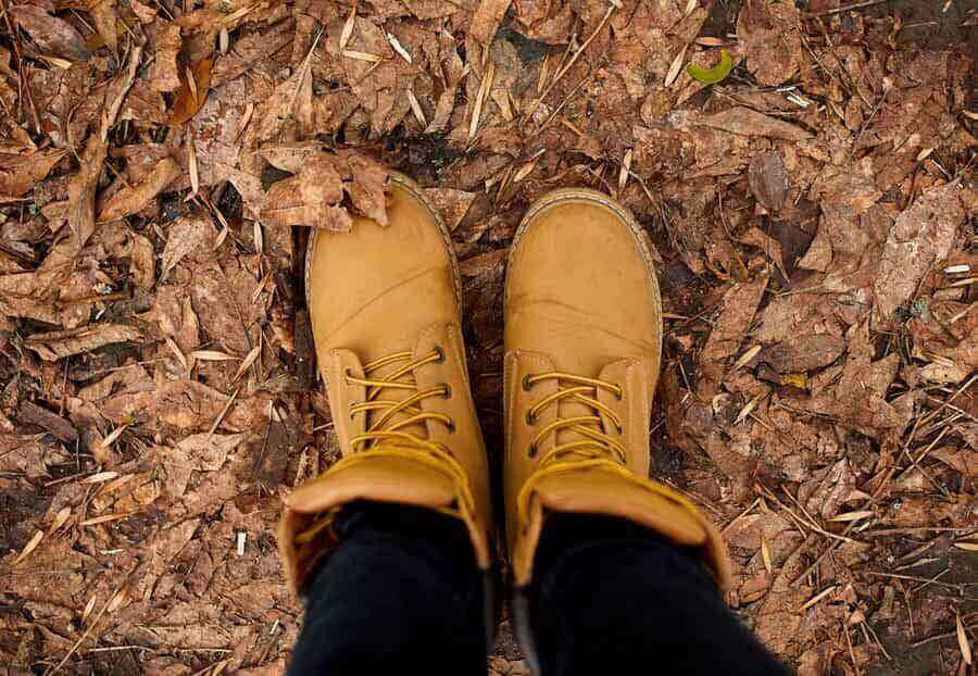 woman standing with hiking boots on autumn leaves